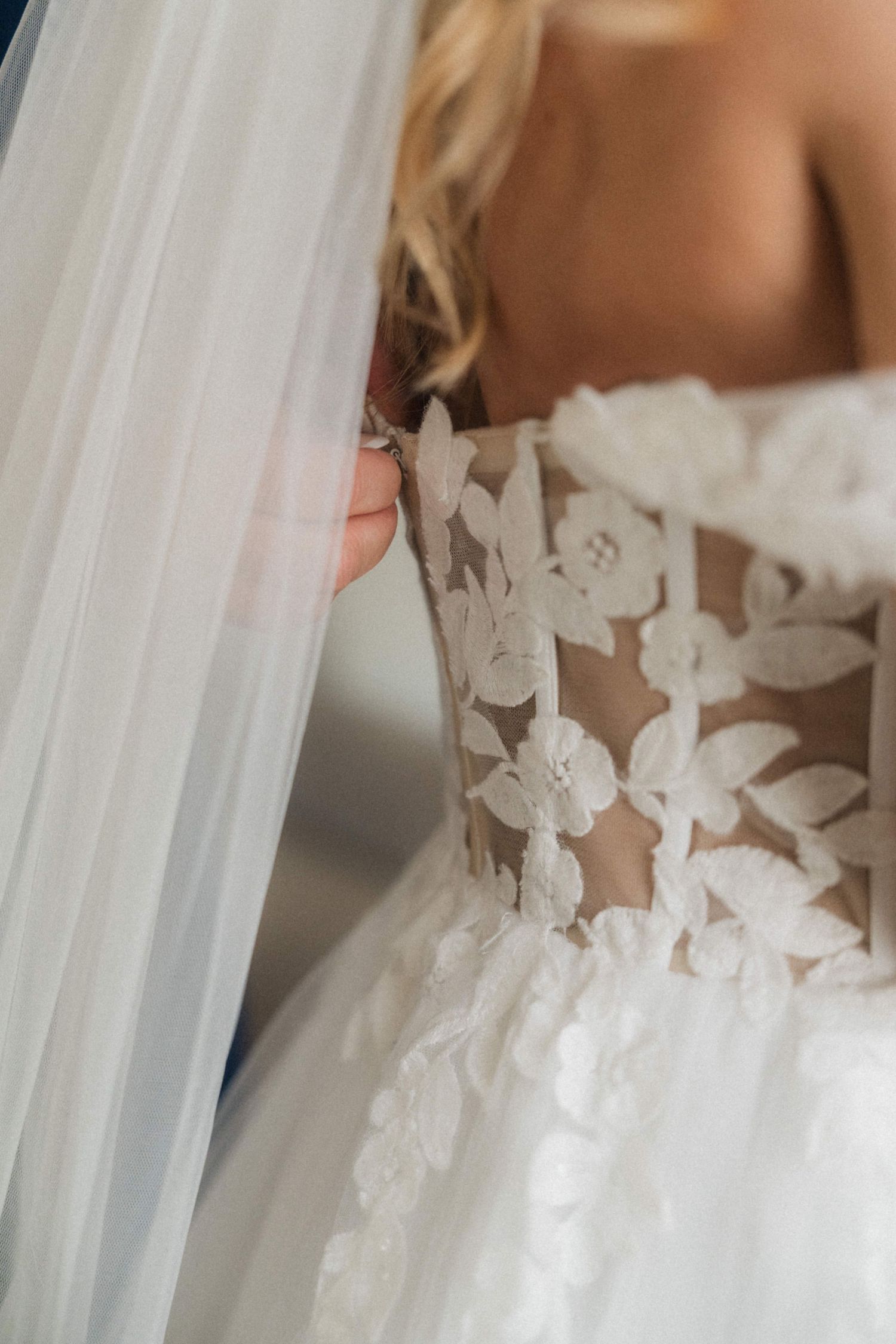 Close-up of a bride's lace floral wedding dress bodice with a flowing white veil draped over her shoulder.
