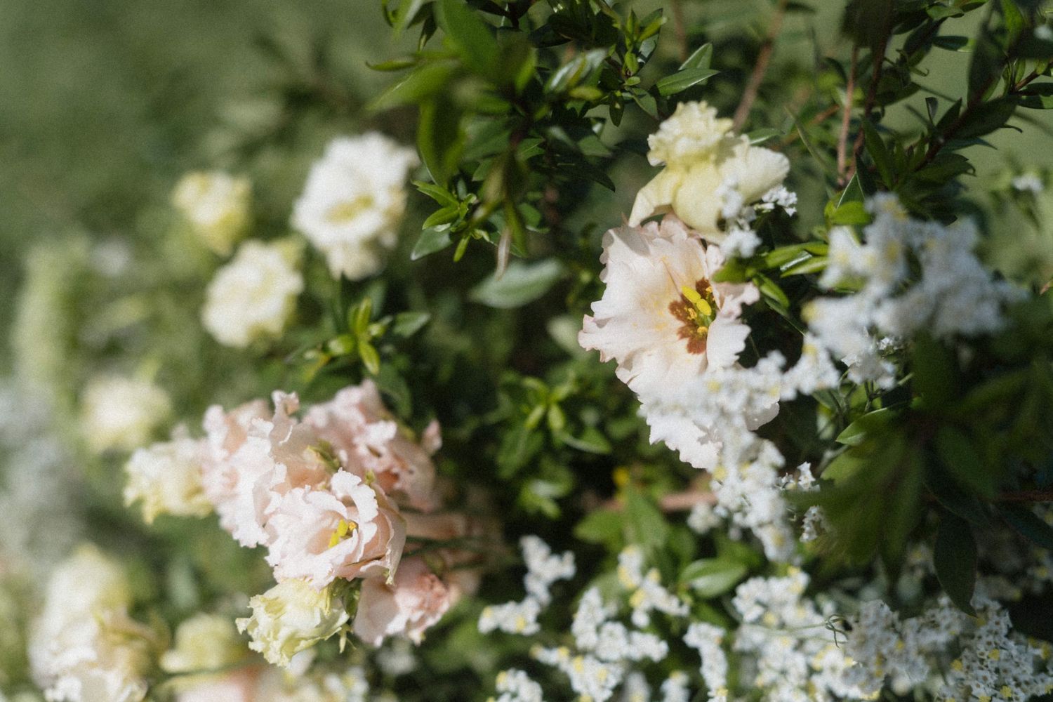 Close-up of elegant wedding floral arrangement featuring soft pink roses, white blooms, and lush green foliage.