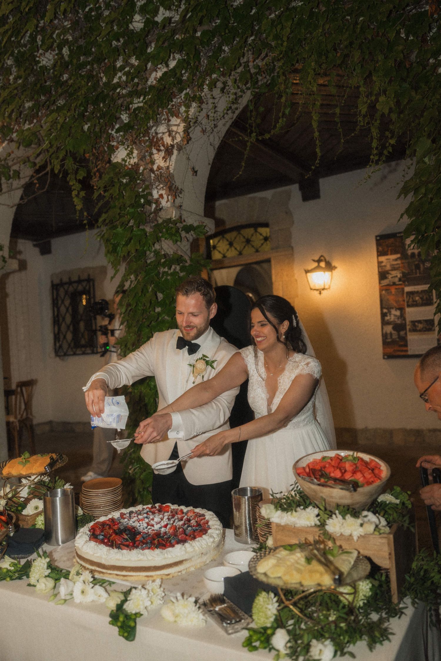 Smiling bride and groom cut their wedding cake surrounded by berry tarts and floral decorations.