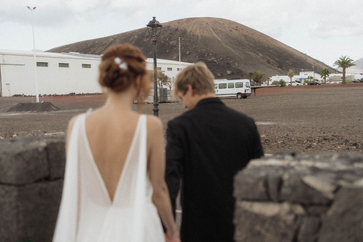 Bride and groom holding hands facing a volcanic landscape on their wedding day in Lanzarote, Canary Islands.