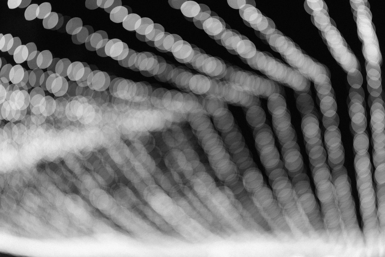 Black and white bokeh abstract photography featuring blurred circular lights arranged in diagonal streaking patterns.