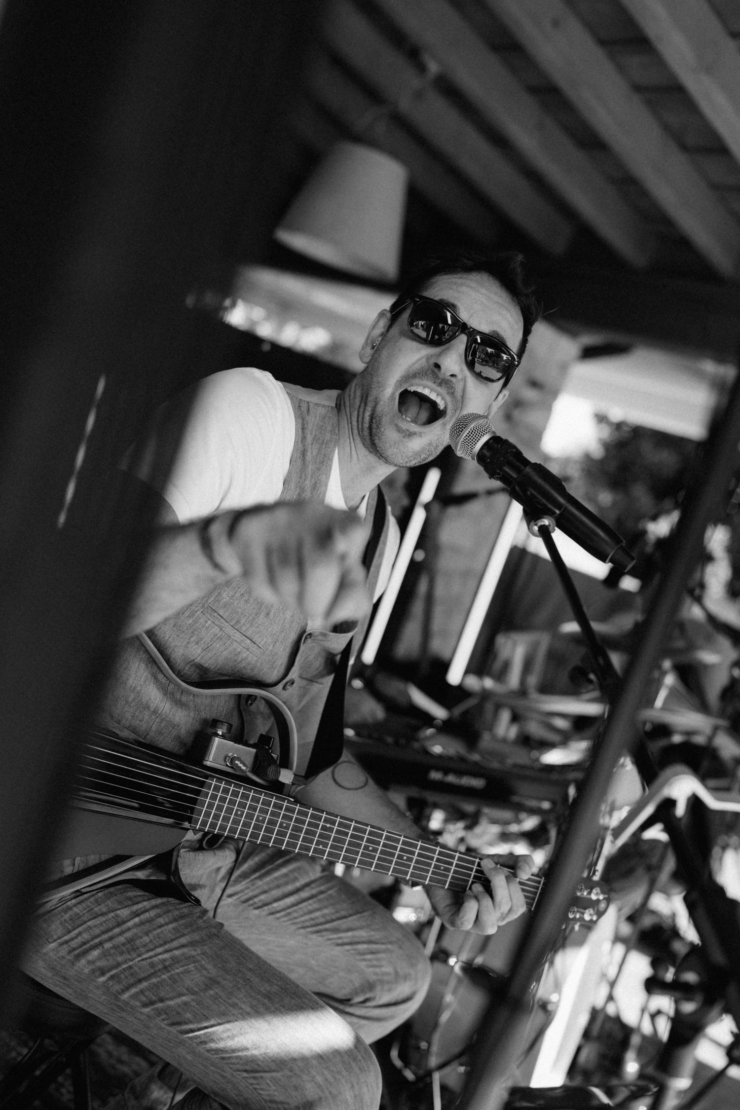 Black and white photo of a male guitarist singing passionately into a microphone while playing guitar outdoors.