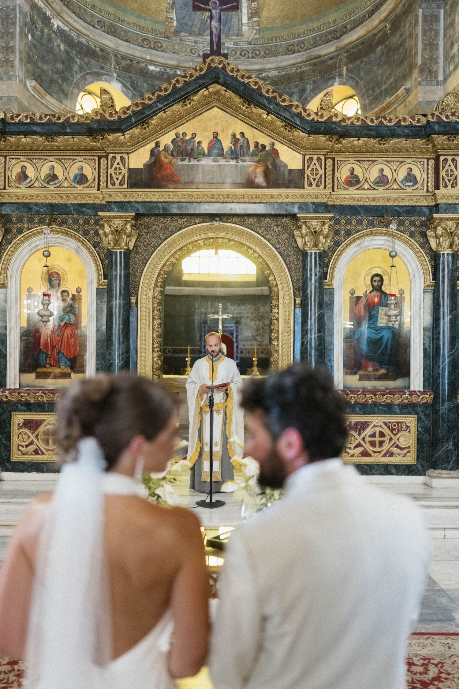 Couple stands before Orthodox priest at ornate church altar during traditional wedding ceremony.