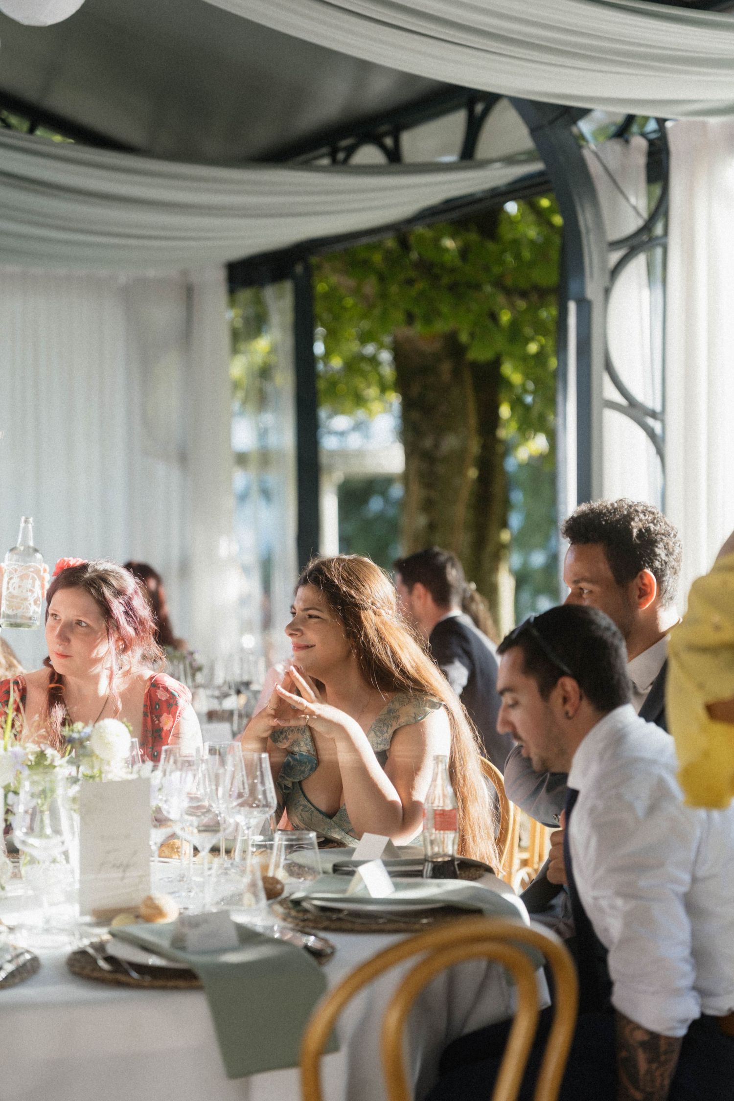 Wedding guests laughing and enjoying conversation at an elegantly set reception table inside a bright, airy venue.
