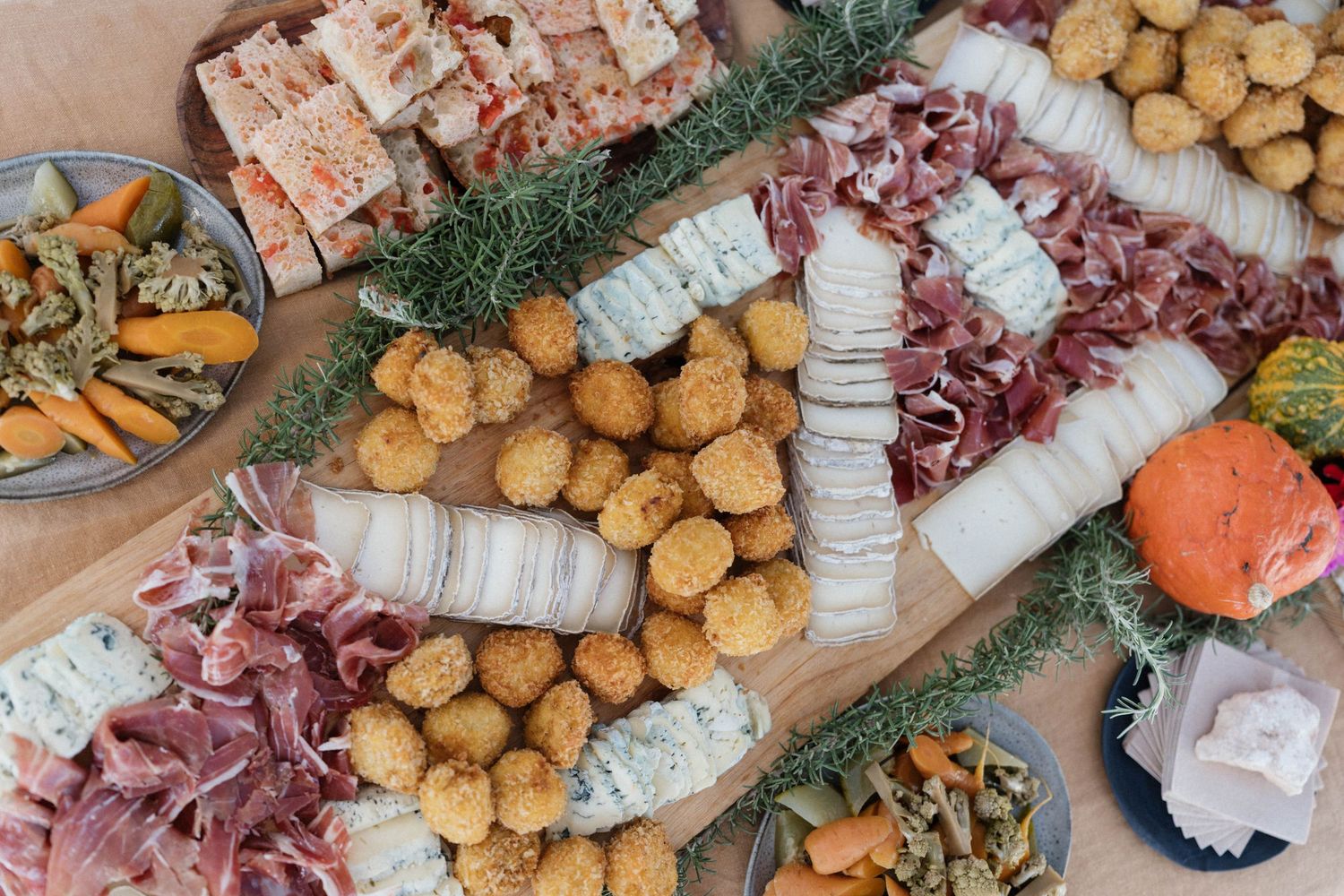 Rustic wooden charcuterie board with sliced cured meats, fried croquettes, cheese, rosemary sprigs, roasted vegetables and a cantaloupe half