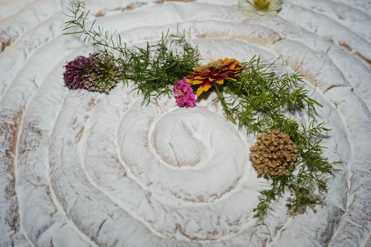 A swirled white plaster surface decorated with dried flowers, rosemary sprigs and a pine cone as rustic wedding table decor.