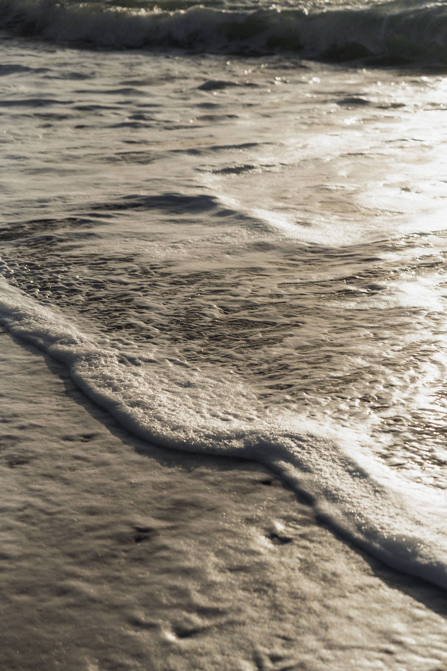 Soft golden ocean waves washing gently onto sandy shore in warm sunlight at beach wedding location.