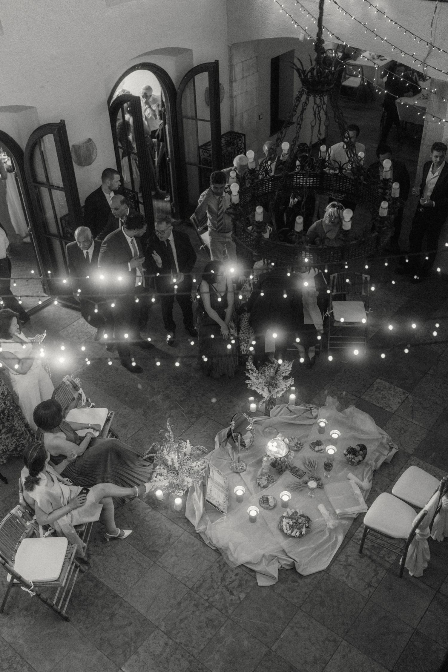 Aerial black and white view of wedding reception with string lights and guests.