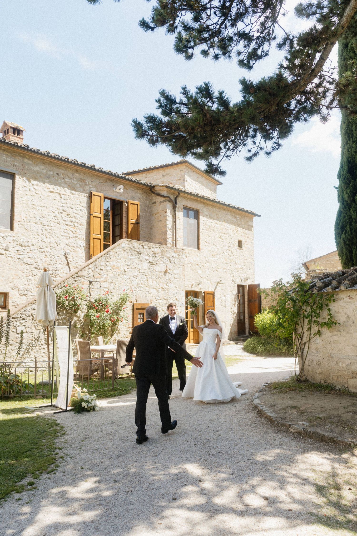 Bride and groom greet a guest outside a rustic stone villa during an outdoor wedding in Tuscany.