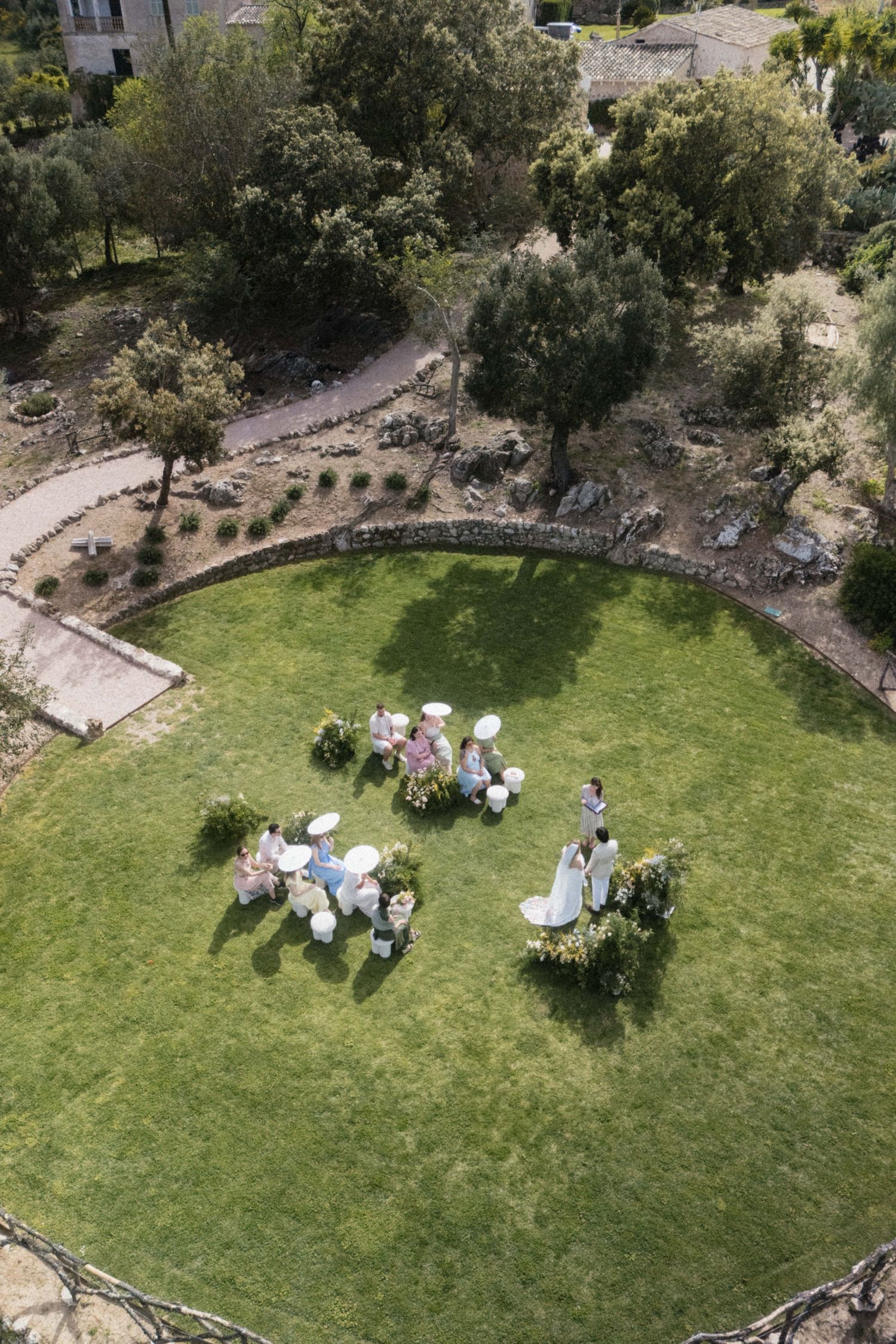 Aerial view of an intimate outdoor wedding ceremony on a circular lawn surrounded by lush greenery.