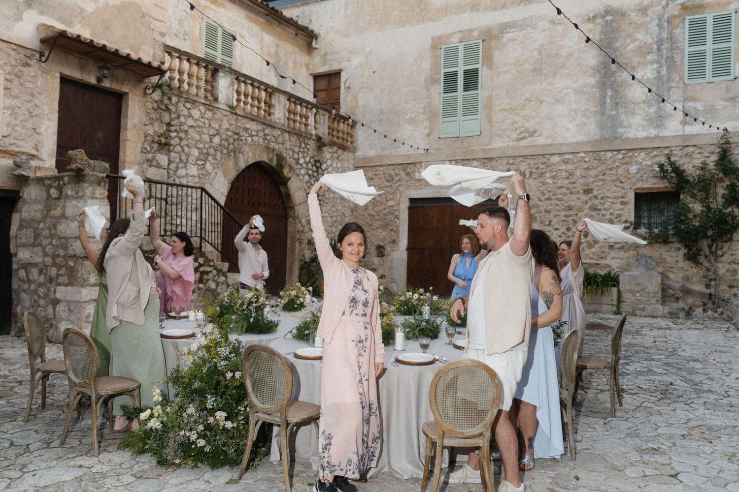 Guests celebrate outdoors at a rustic stone villa courtyard wedding reception with floral table decor.