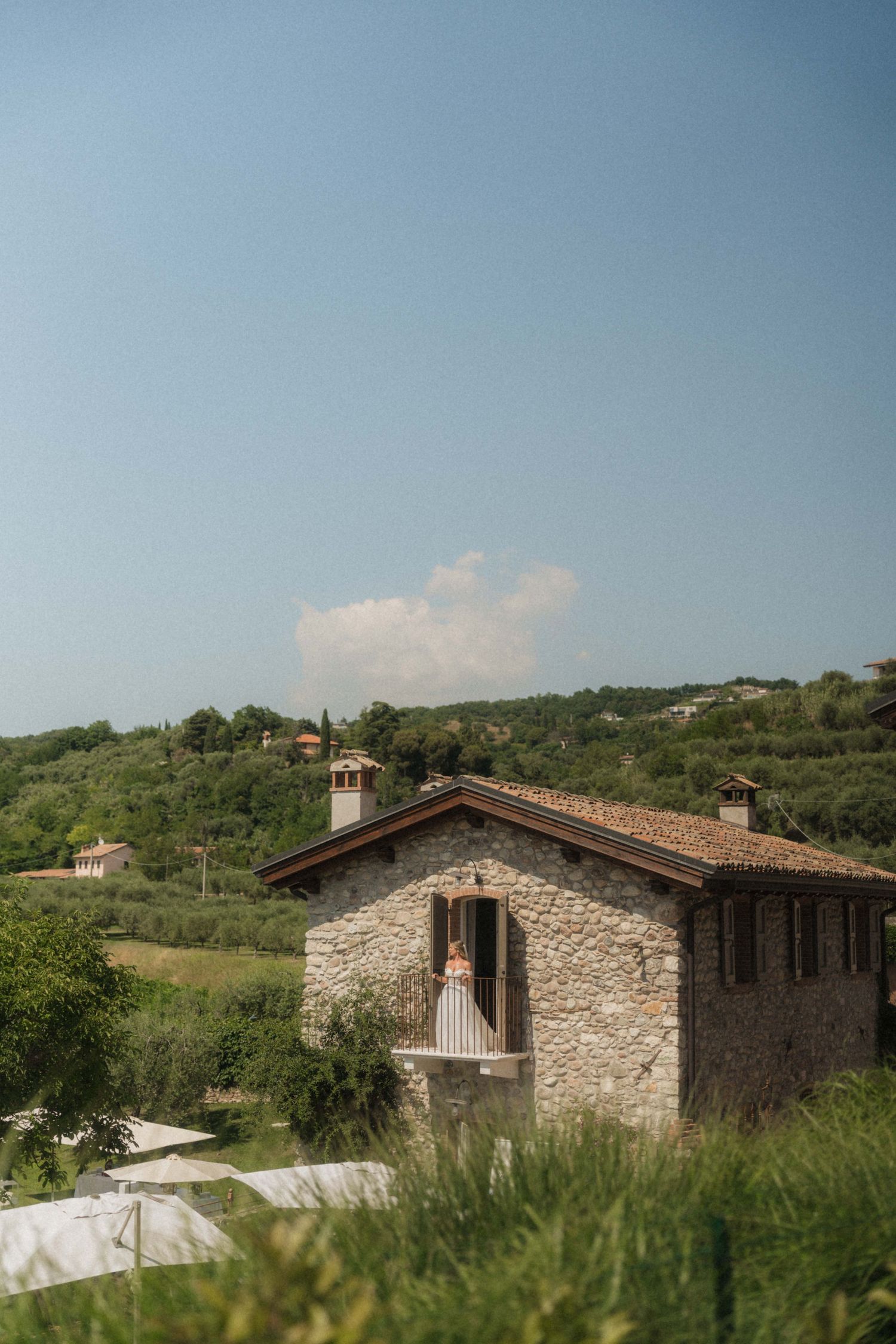 A rustic stone villa nestled among lush green hills under a clear blue sky in the Italian countryside.