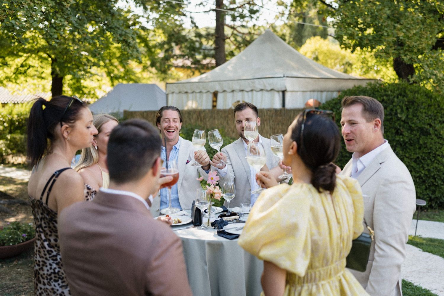 Elegant outdoor garden party with guests raising glasses in a toast around a decorated table.
