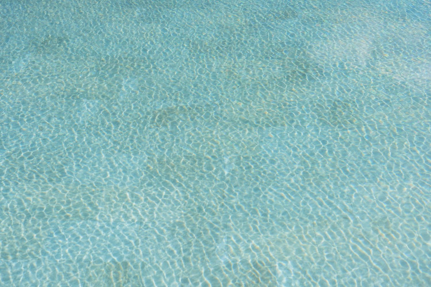 Clear turquoise water with gentle ripples and sunlight patterns dancing across a sandy bottom in a calm tropical sea.