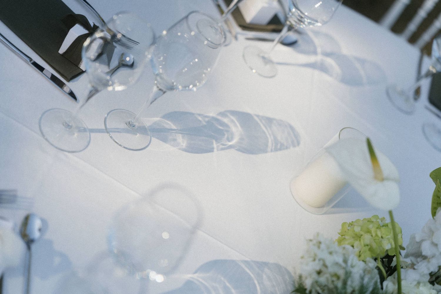 Elegant white tablecloth with crystal wine glasses and candles casting soft shadows at a formal event.