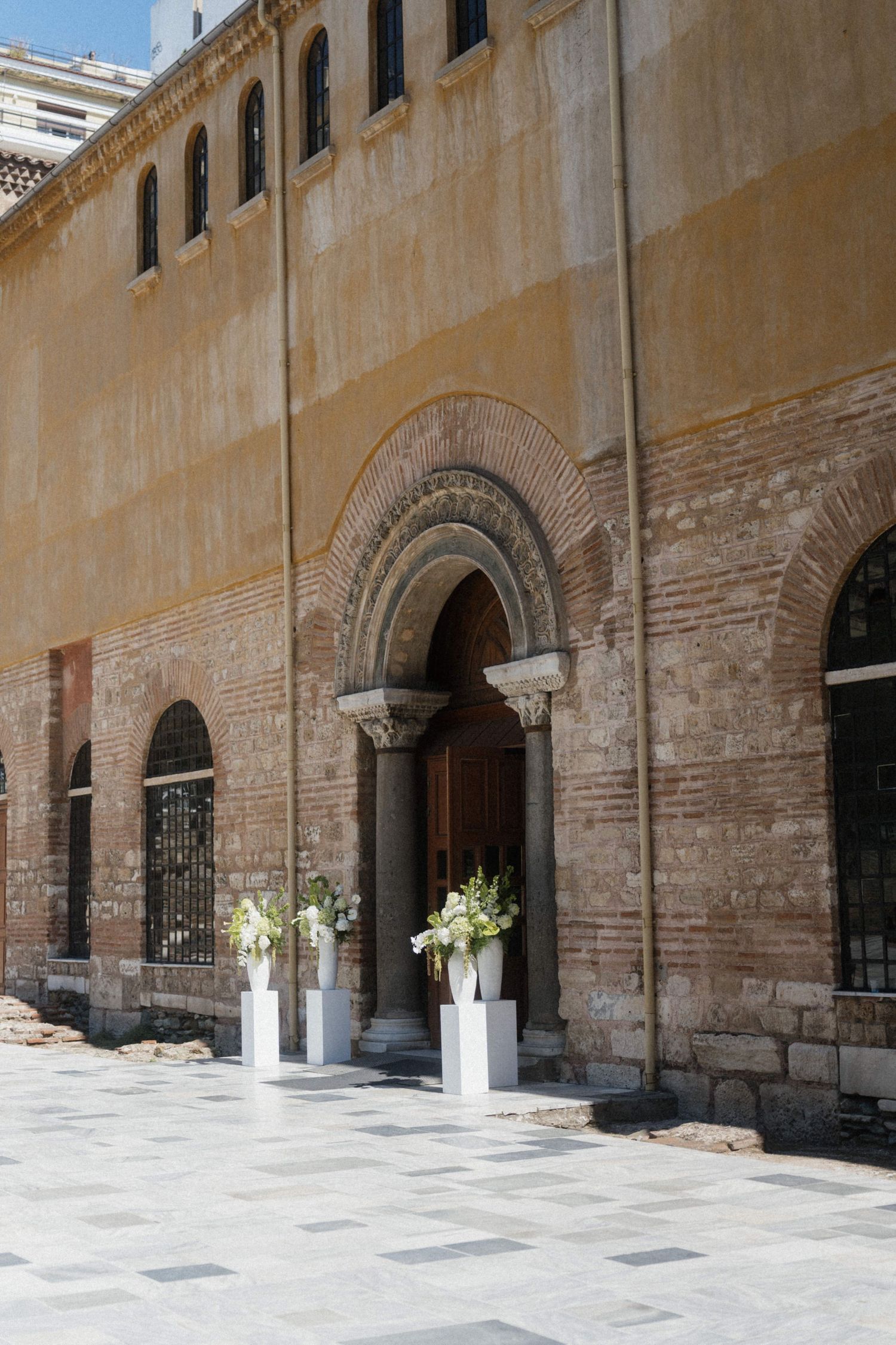 Ancient Byzantine church entrance decorated with white floral arrangements on pedestals.