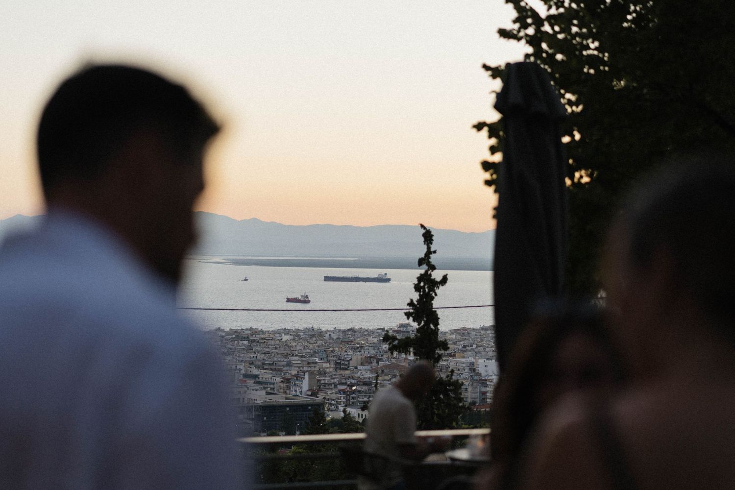 Couple enjoying a romantic sunset view of Thessaloniki cityscape and sea from an elevated viewpoint at dusk.