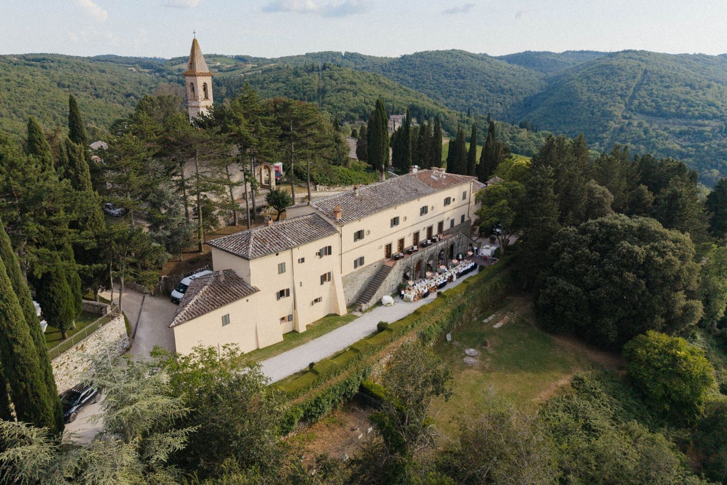 Aerial view of elegant Italian villa wedding venue surrounded by cypress trees and rolling Tuscan hills.