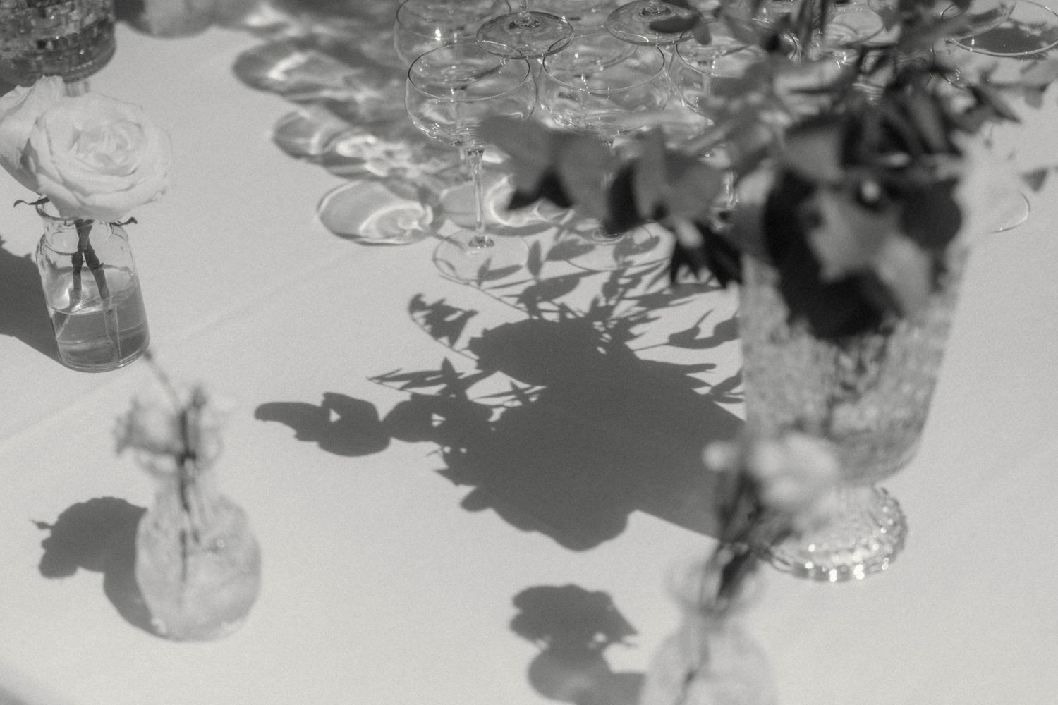 Black and white photo of wedding table centerpieces with roses and greenery casting shadows on linen.