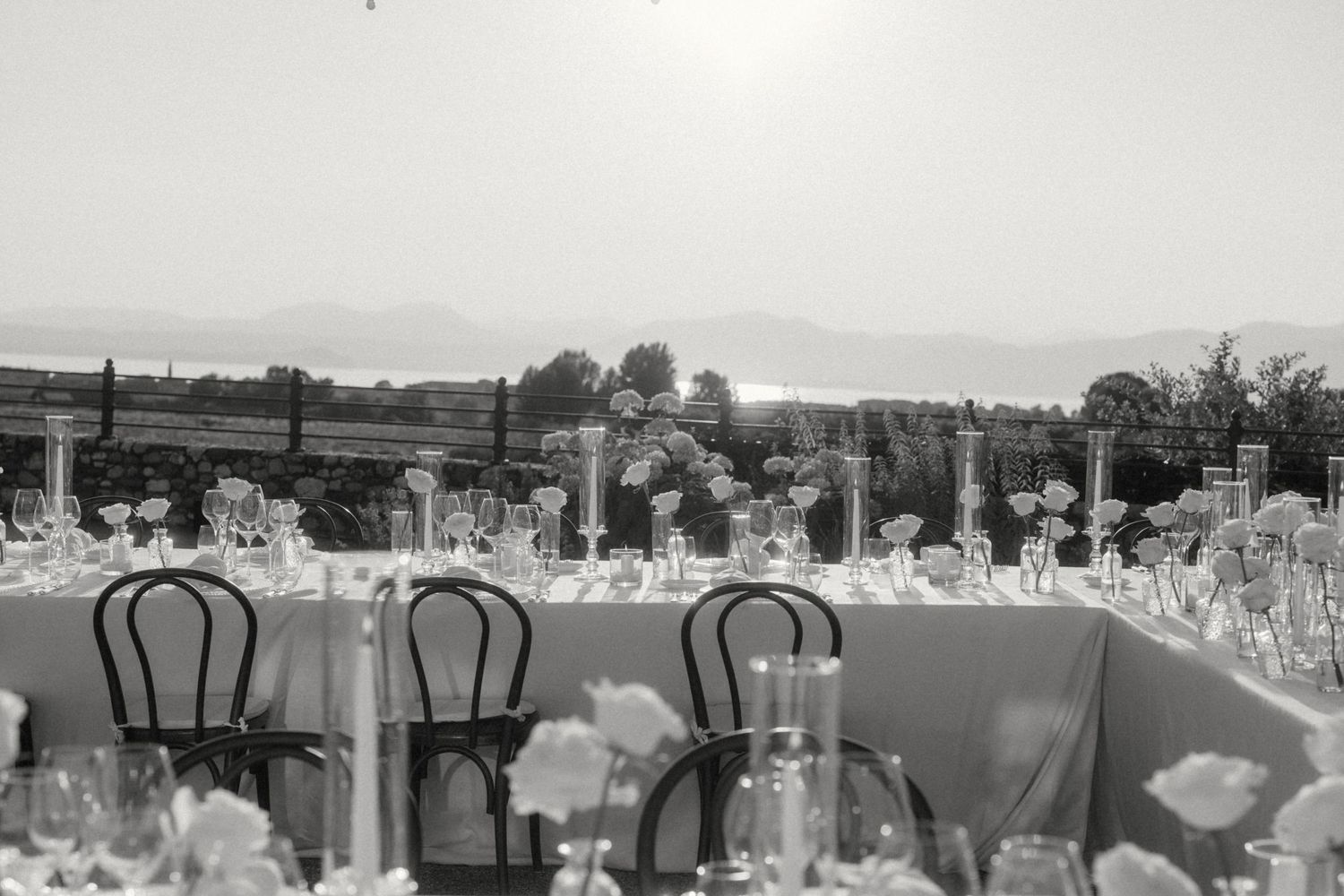 Black and white photo of elegant outdoor wedding reception table with candles and scenic landscape view.