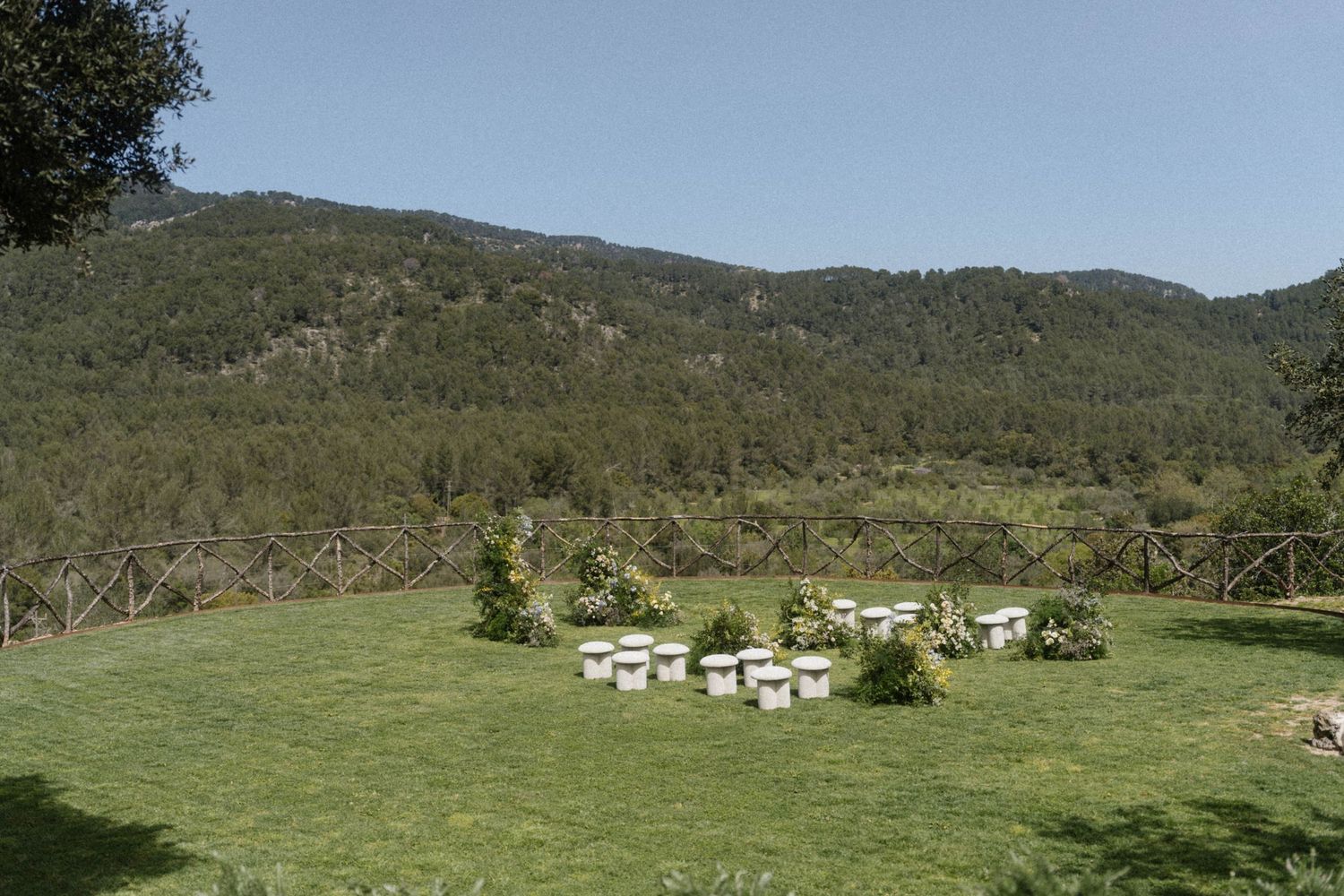 Beehives on green lawn with mountain forest backdrop under clear blue sky.