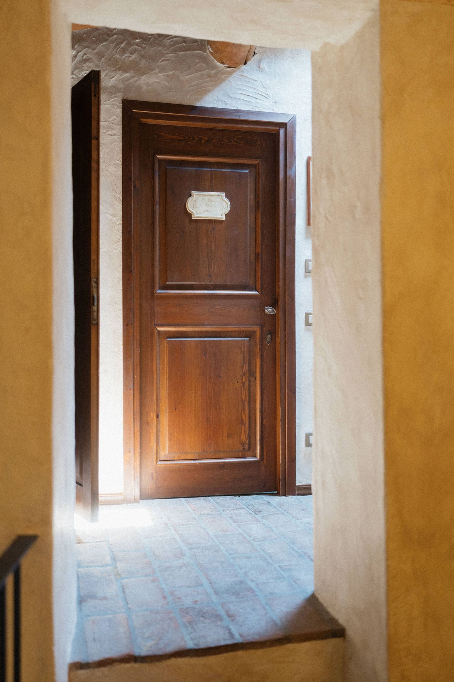 Rustic hallway with warm yellow walls leading to a classic wooden door with decorative panel.