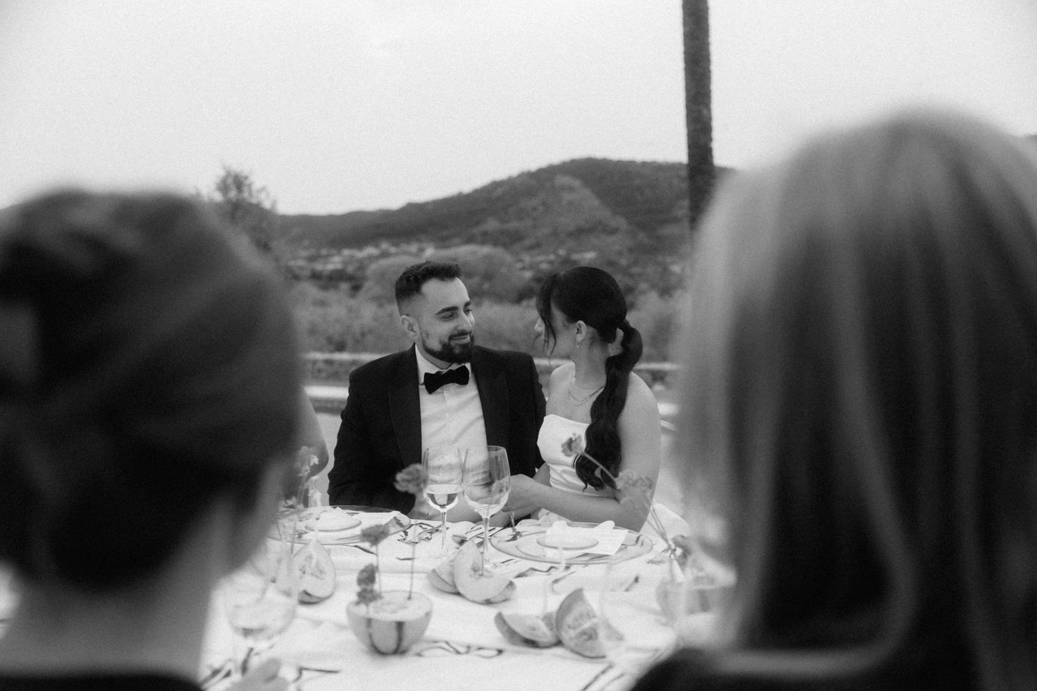Black and white wedding photo of bride and groom sharing an intimate moment at the reception dinner table.