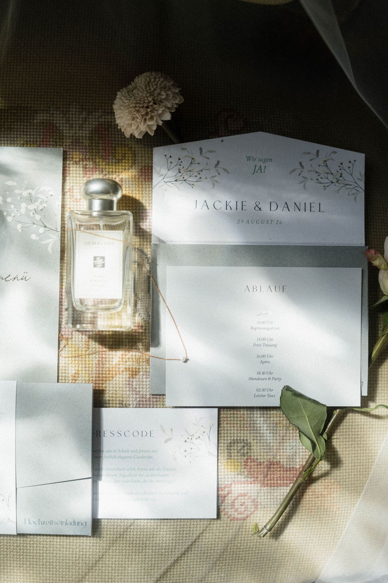 Luxury wedding stationery flatlay featuring Jo Malone perfume, floral invitations, and elegant menu cards in soft light.
