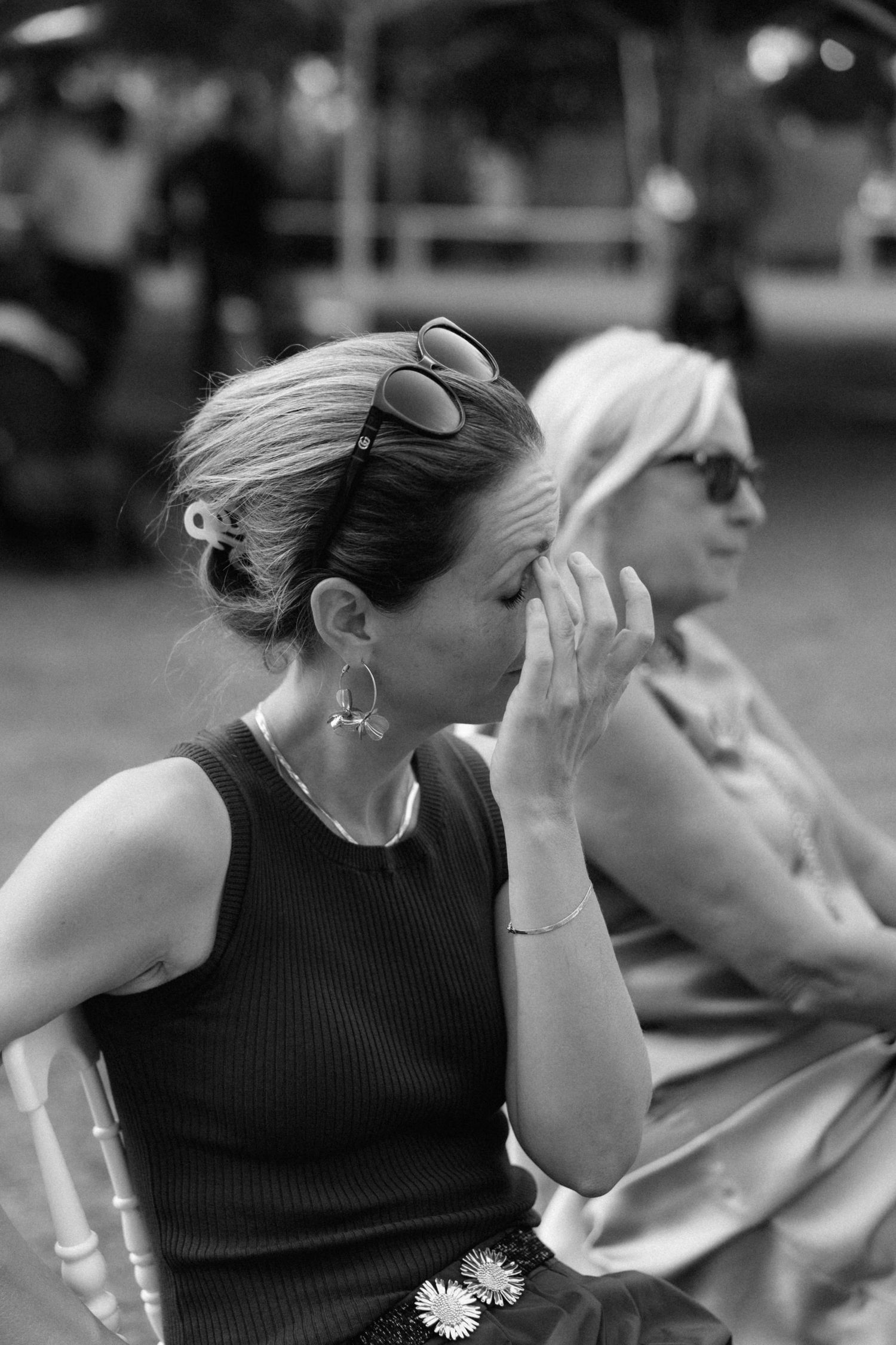 Black and white photo of emotional female wedding guest wiping tears while seated at an outdoor ceremony.