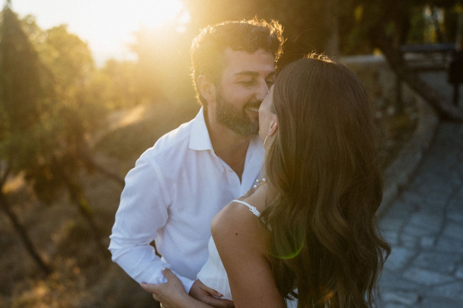 Romantic couple sharing a tender moment at golden sunset in a vineyard, bathed in warm backlight.