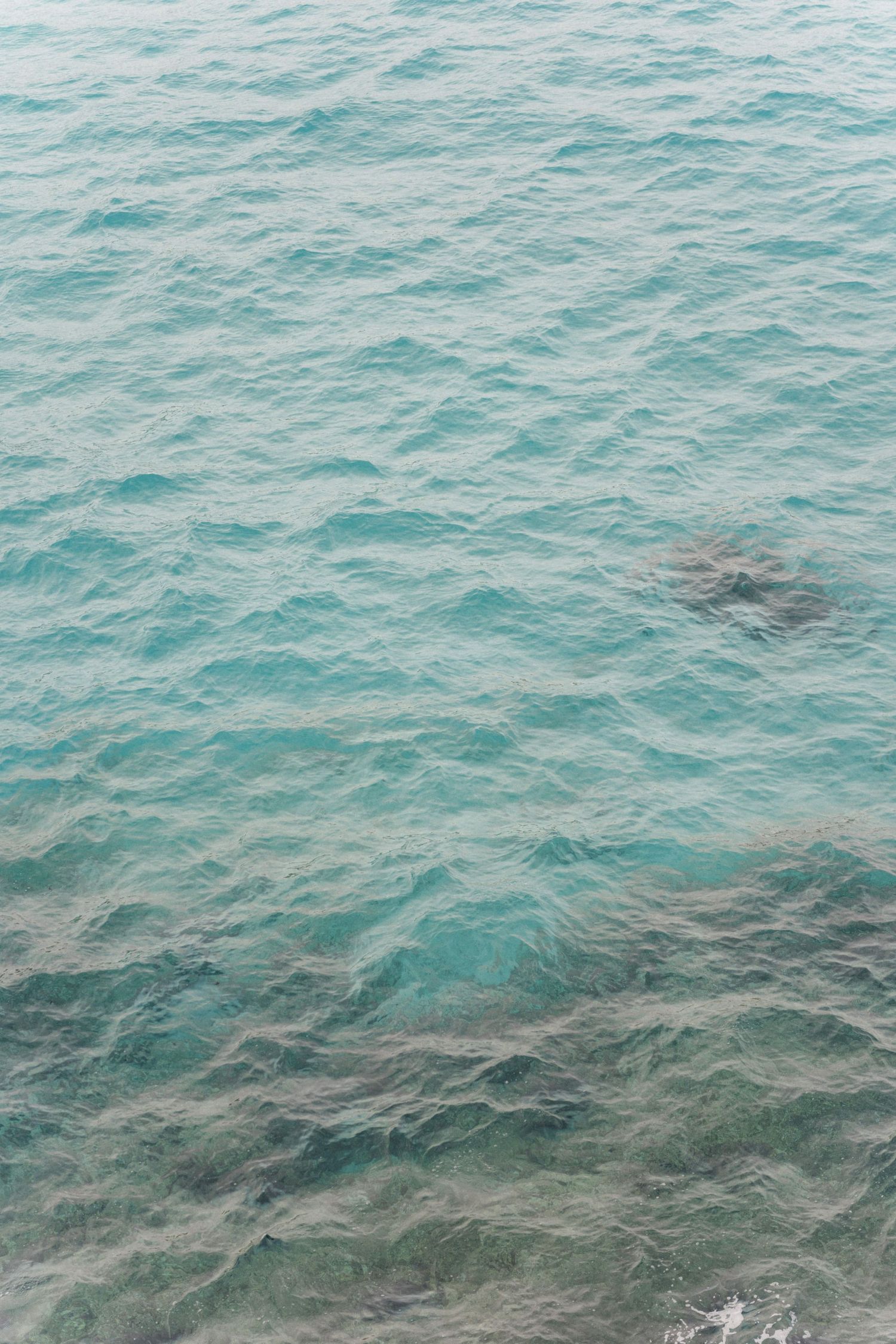 Calm turquoise sea water with gentle ripples and darker rocks visible beneath the surface.