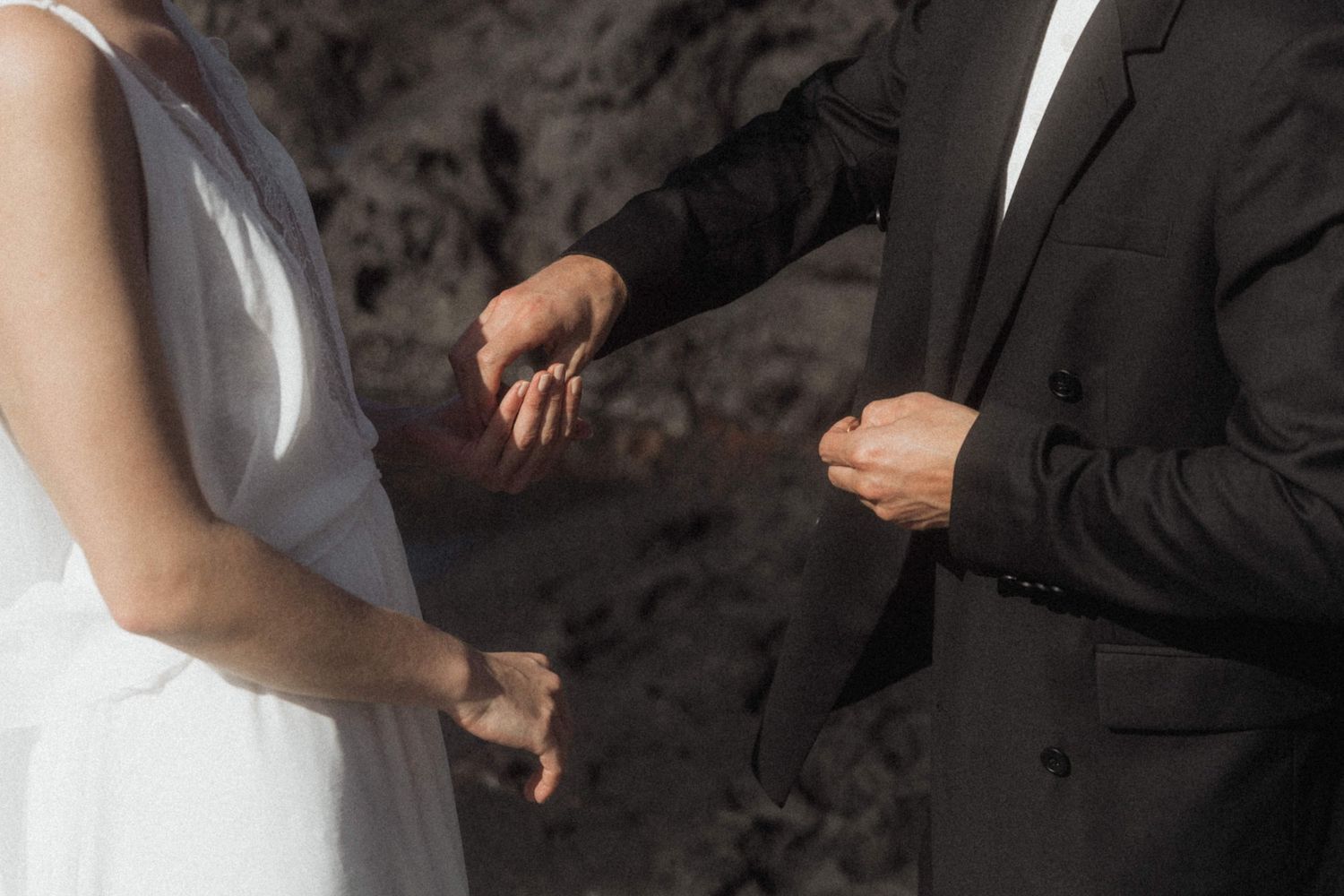 Bride and groom exchanging rings during outdoor wedding ceremony, wearing white dress and black suit.