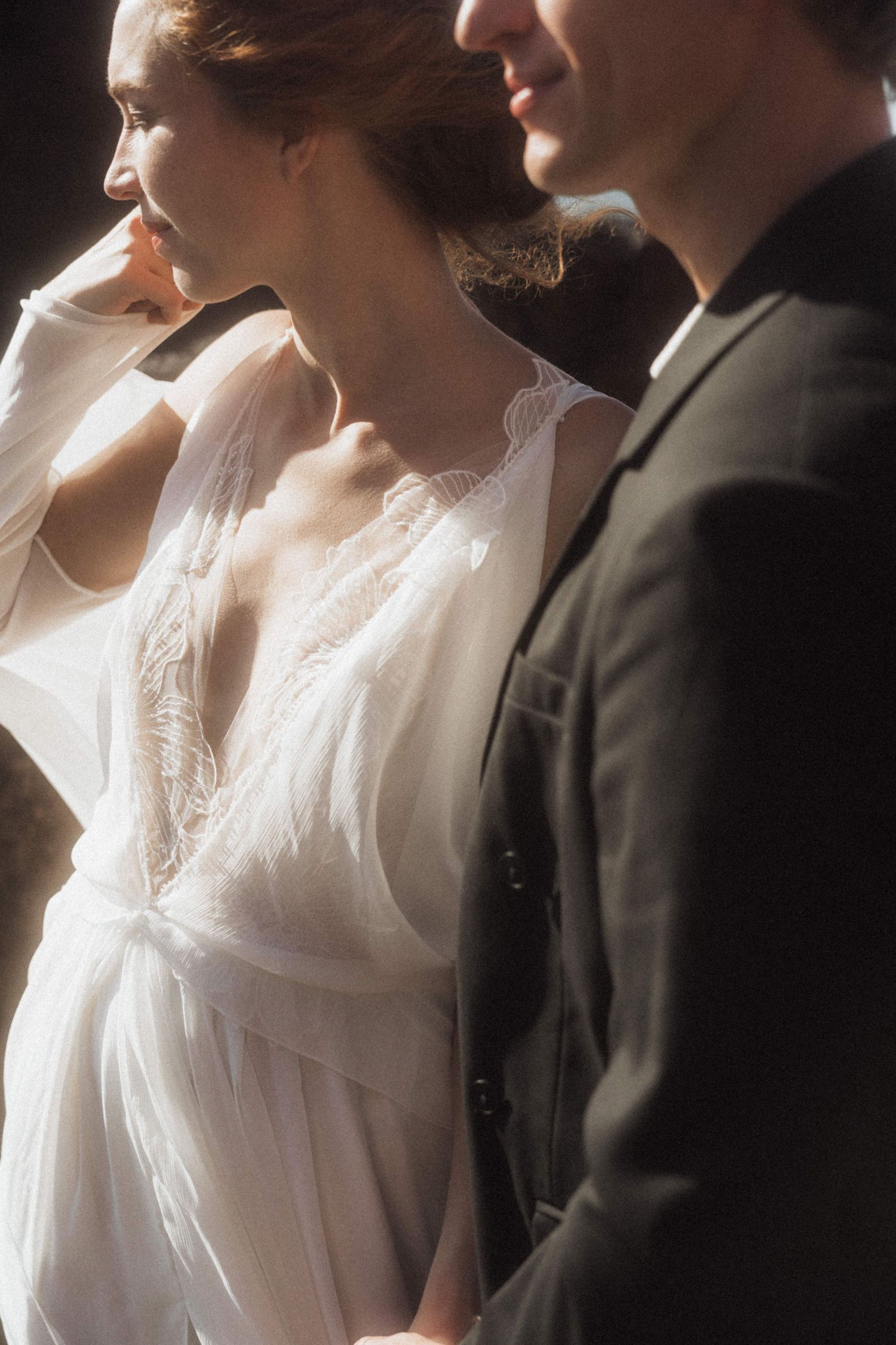 Close-up of bride in white lace gown and groom in dark suit standing together.