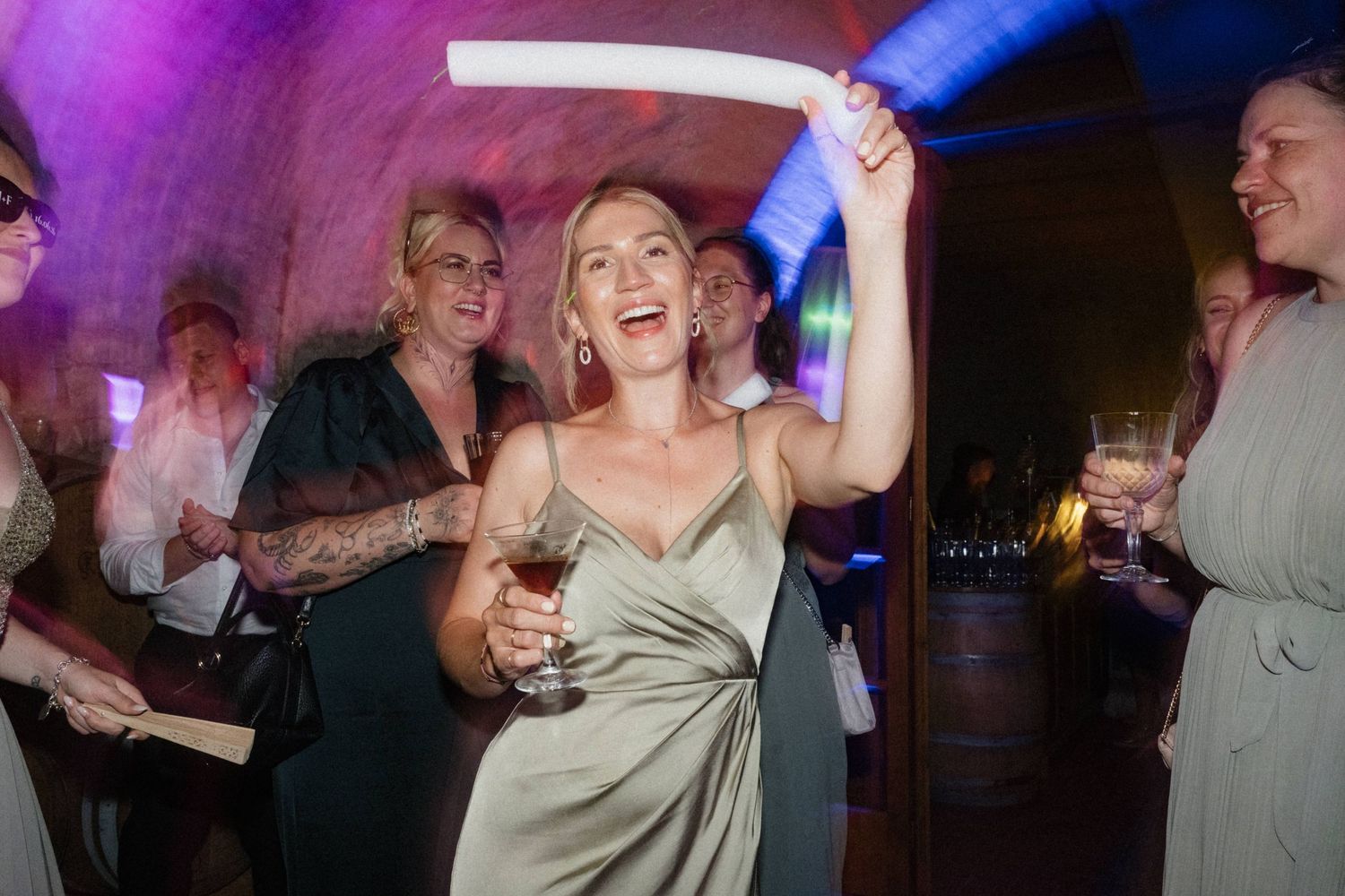 Joyful bridesmaid in sage green dress dancing with glow stick at lively wedding reception party.