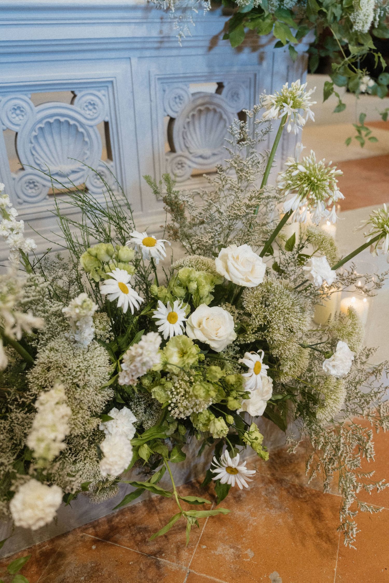 Elegant wedding floral arrangement with white roses, daisies, and greenery beside blue cabinet.