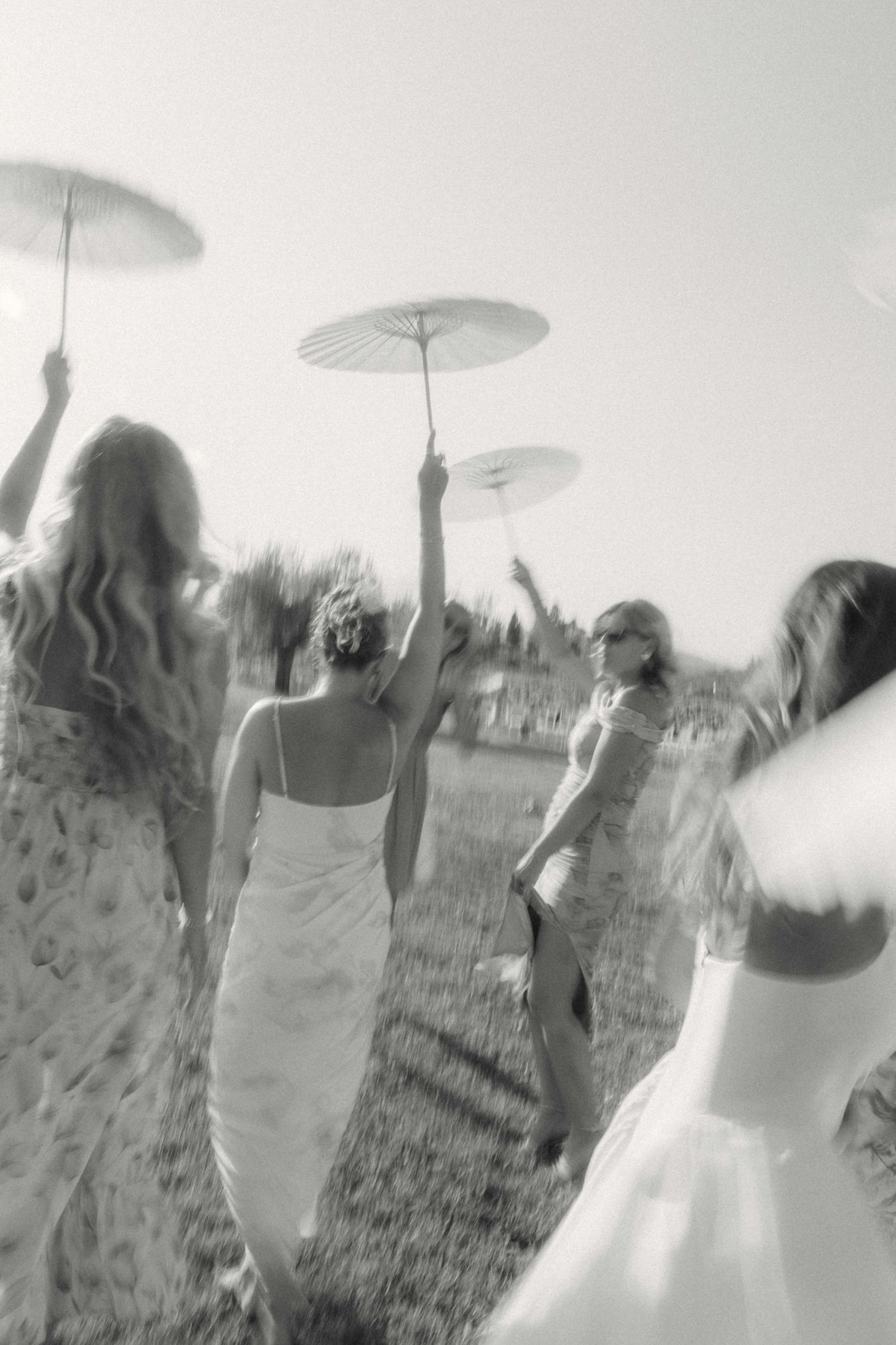 Black and white photo of bridesmaids walking in a field with parasols.