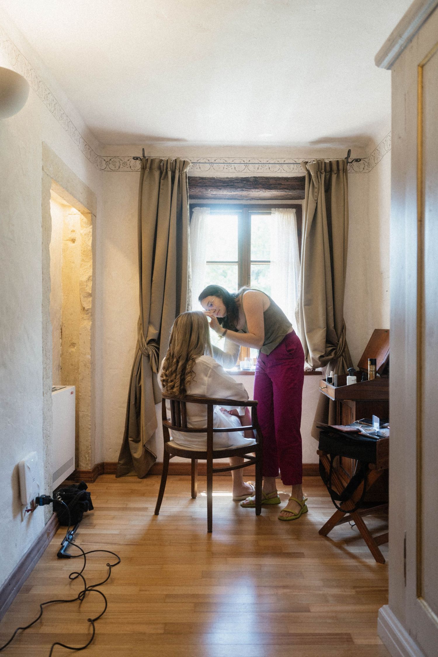 Woman in burgundy pants arranging clothes on a wooden chair in a charming vintage room with hardwood floors.