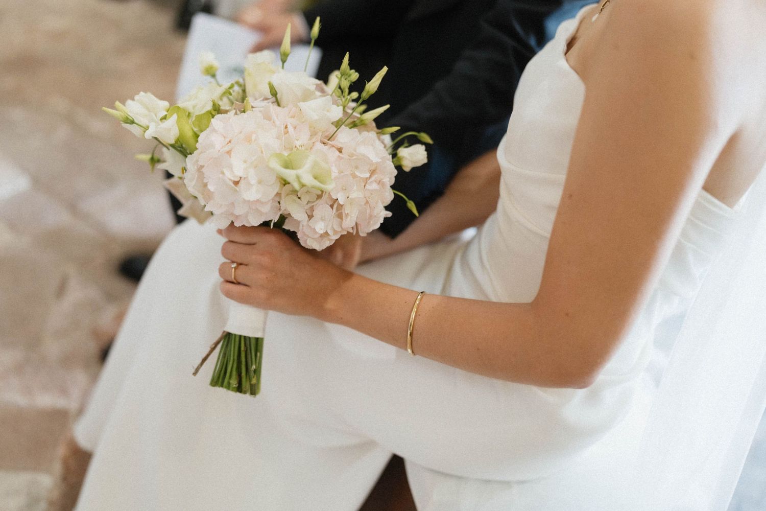 Bride in white dress holding elegant blush pink and white floral wedding bouquet with roses and hydrangeas.