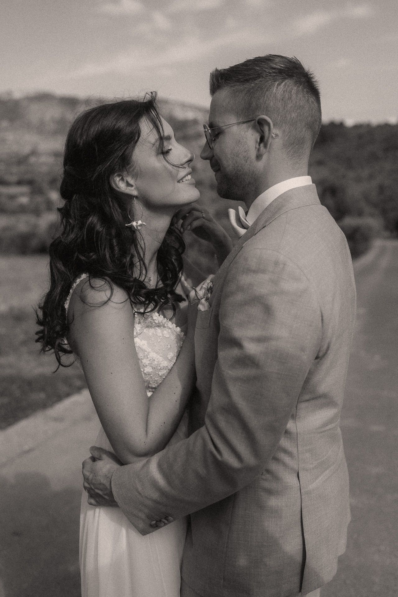 Black and white photo of a smiling bride and groom embracing outdoors on their wedding day.