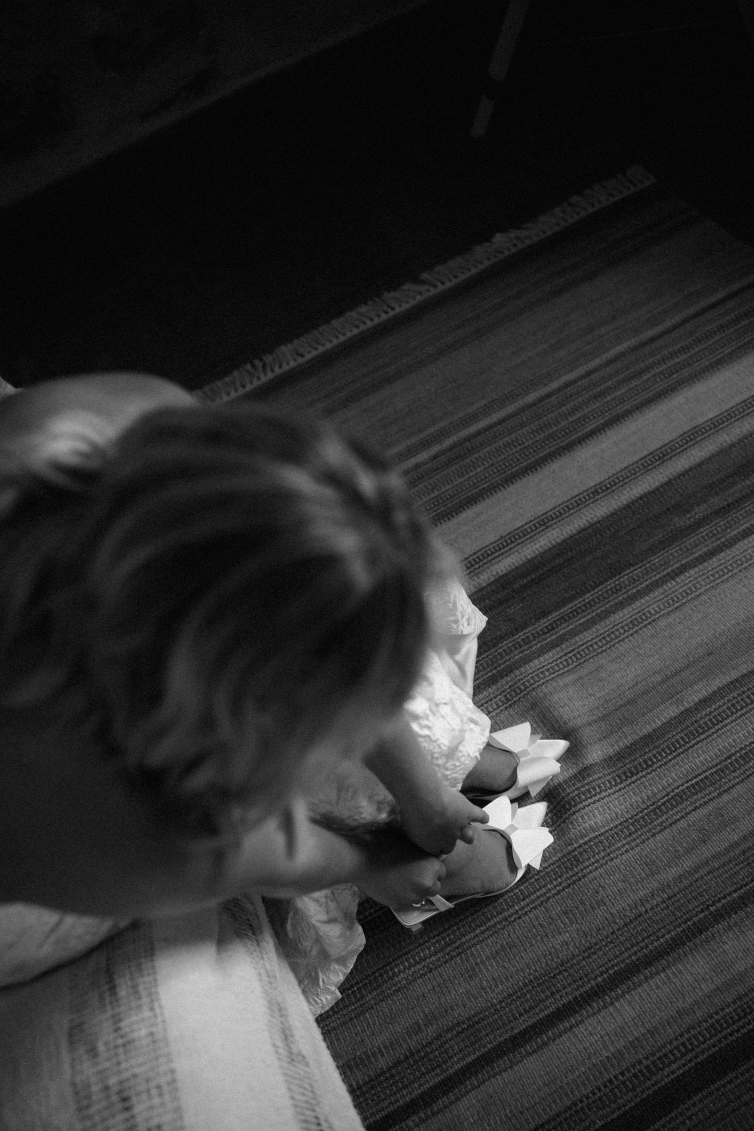 Black and white overhead shot of a bride putting on white wedding shoes on a striped floor.