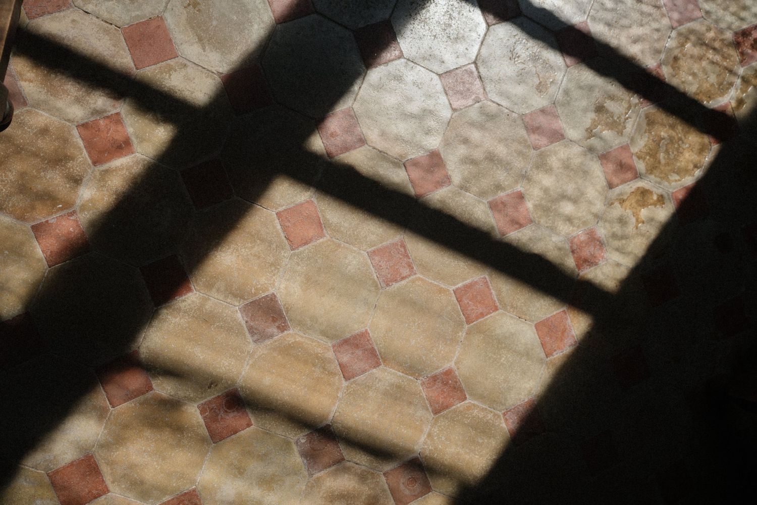 Vintage ceramic floor tiles with geometric patterns casting dramatic shadows in warm terracotta and beige tones.