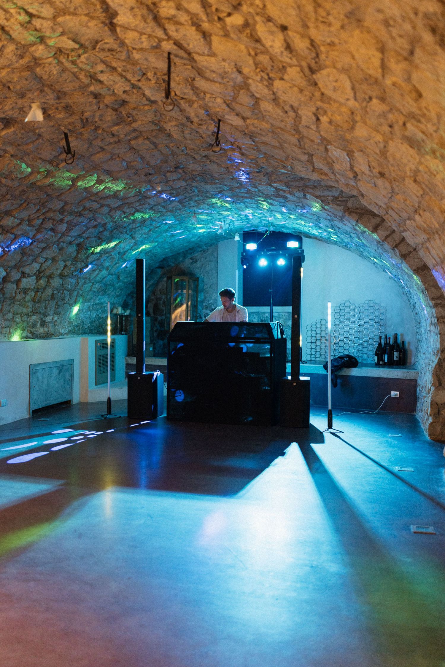 DJ performing in a stunning stone vaulted cellar venue with colorful blue and green lighting effects.