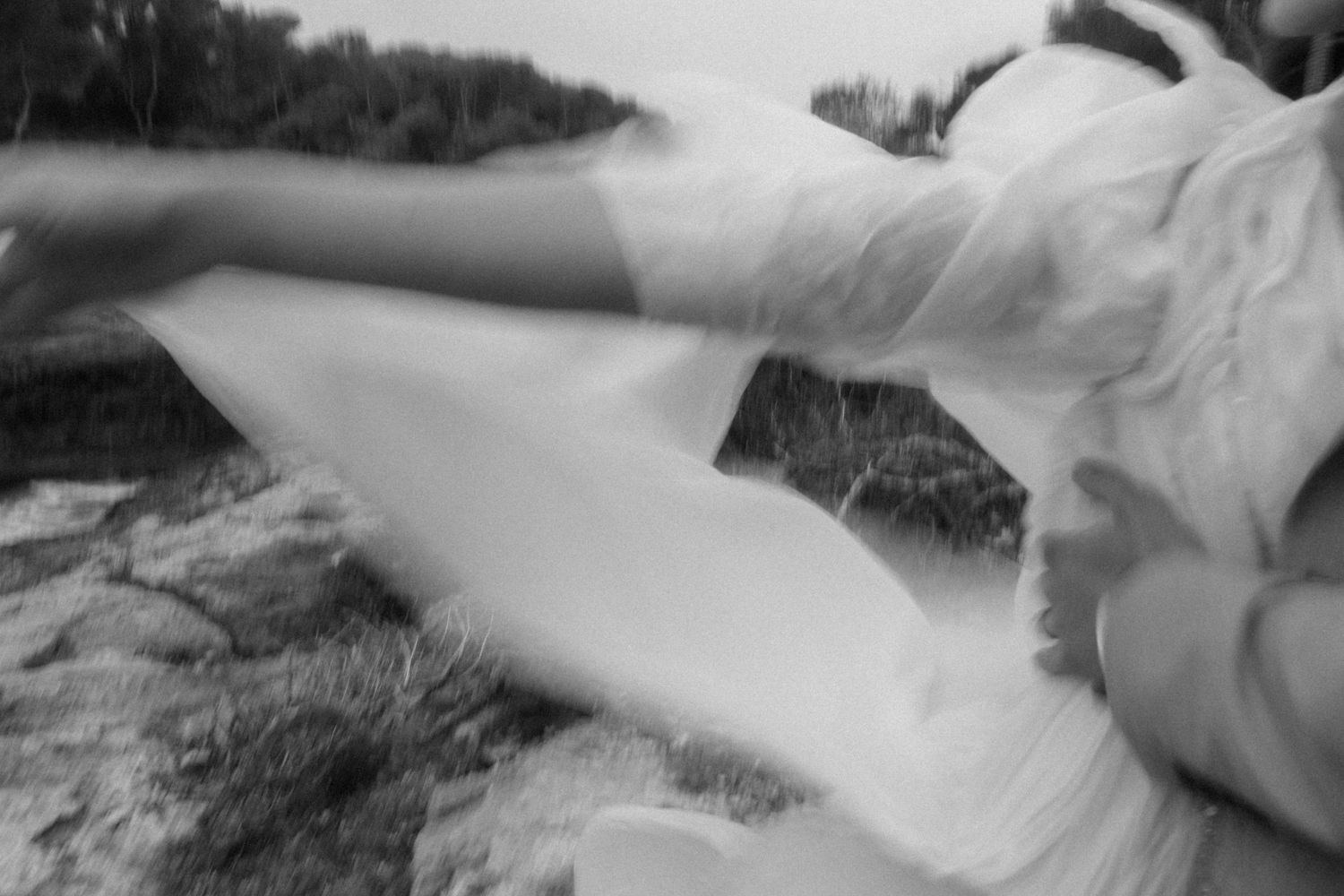 Blurry black and white photo of a bride in a white wedding dress lying on grass outdoors.