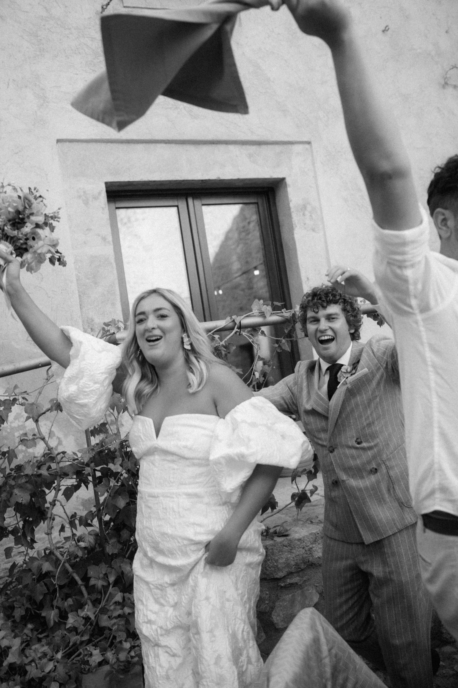 Joyful bride and groom celebrating outdoors at wedding in black and white photo.