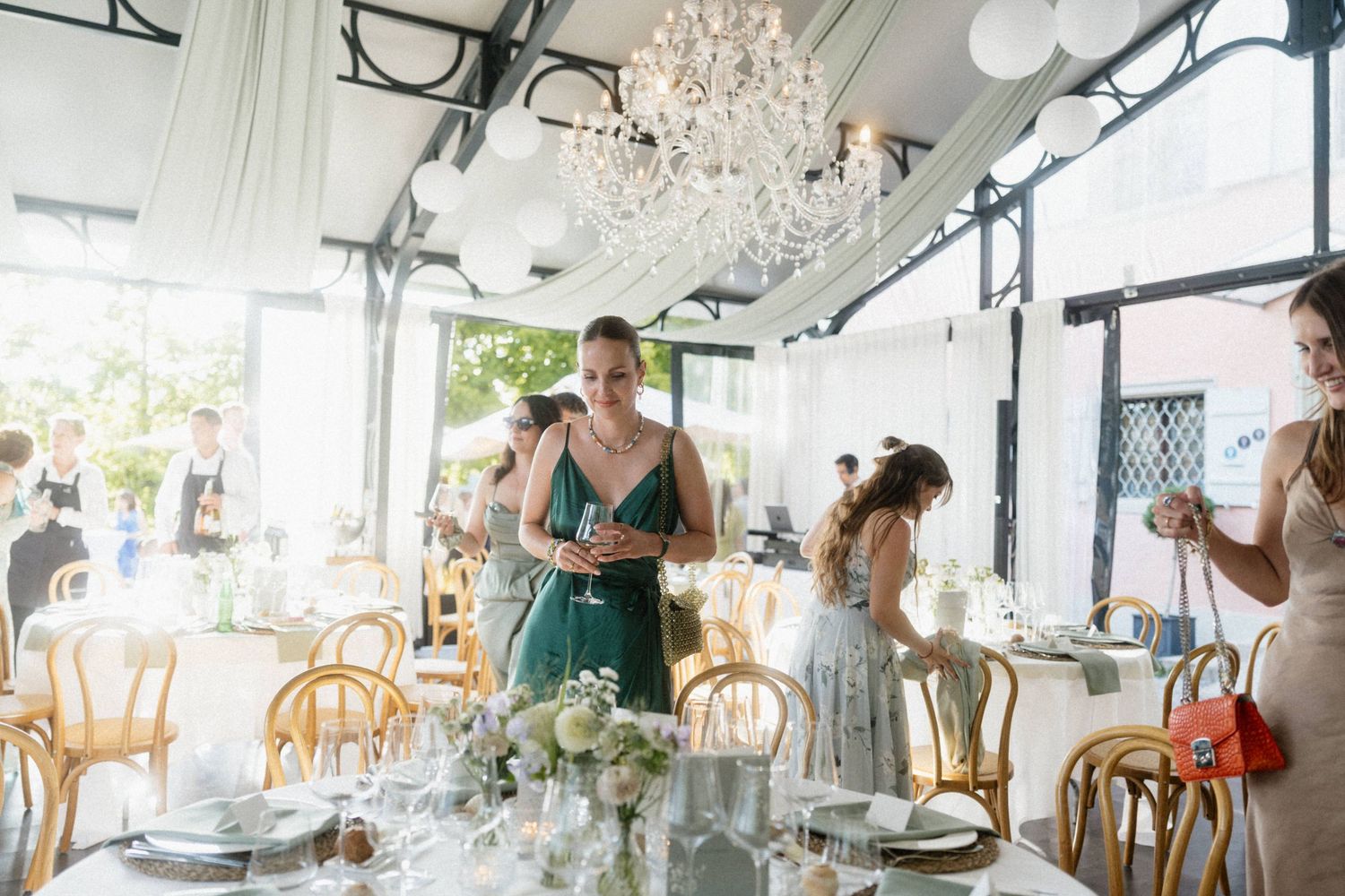 Elegant wedding reception with guests in formal attire gathered around decorated tables under crystal chandeliers.