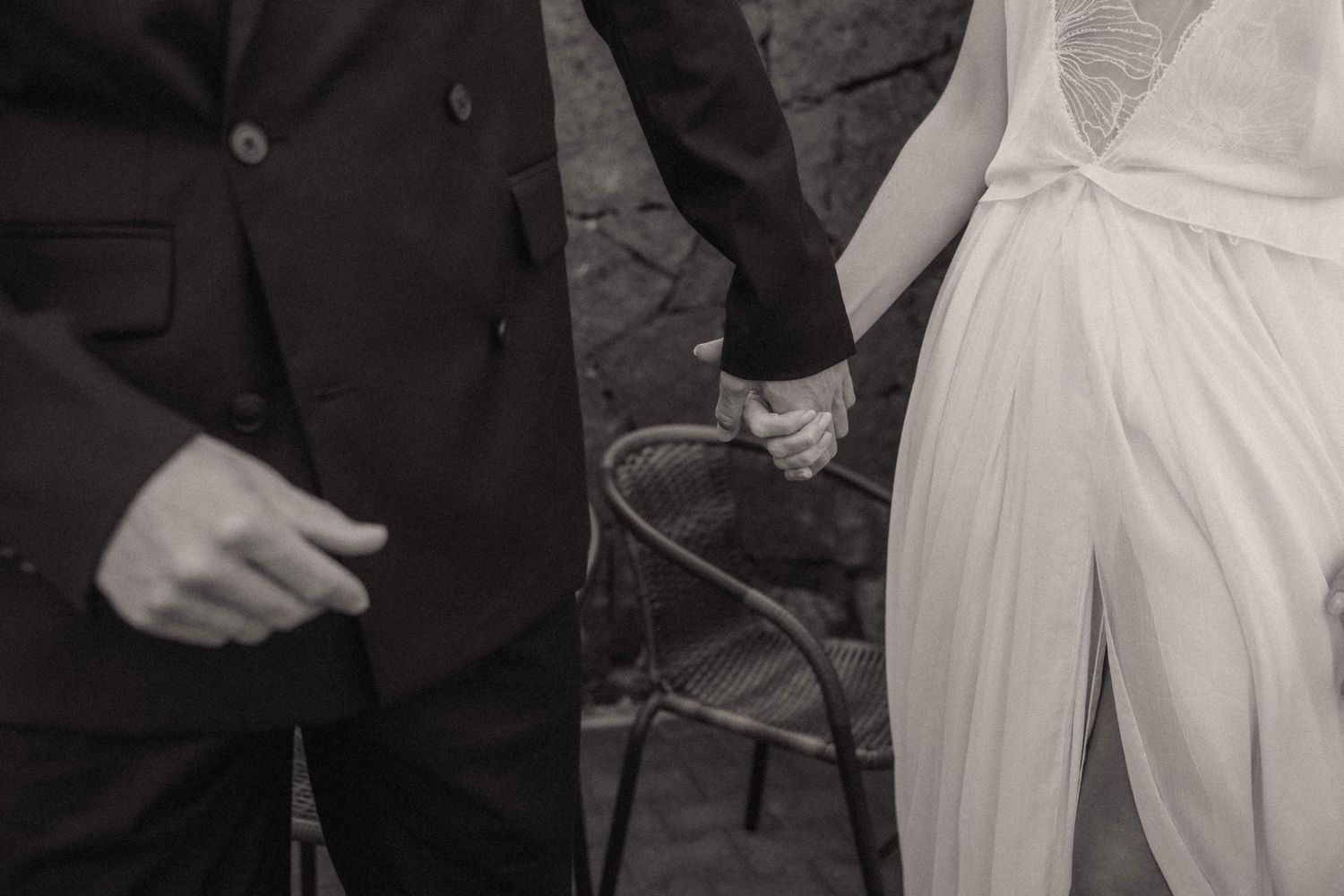 Black and white photo of bride and groom holding hands at wedding ceremony.