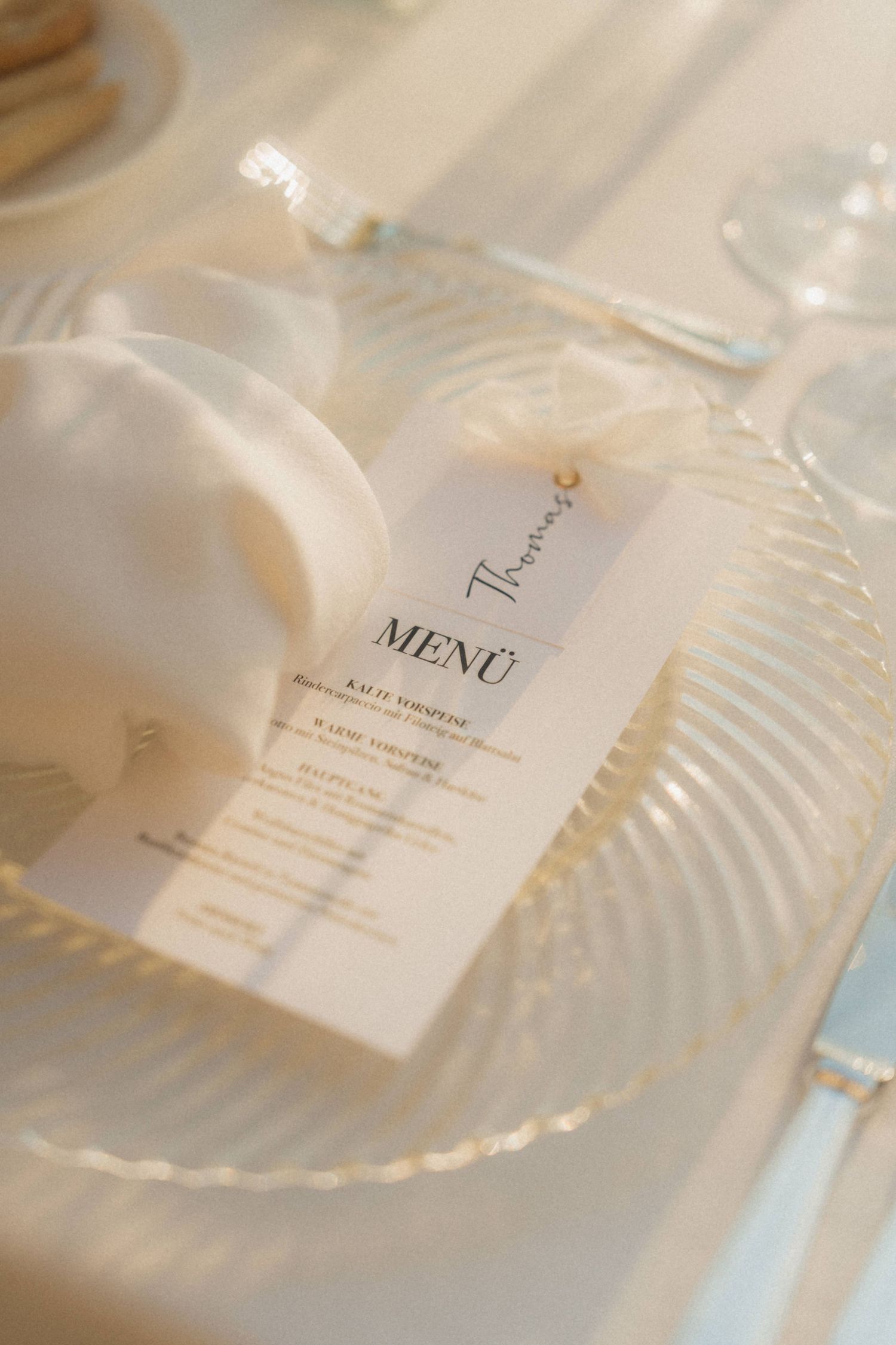 Elegant wedding table setting with glass charger plate, white napkin, and personalized menu card.