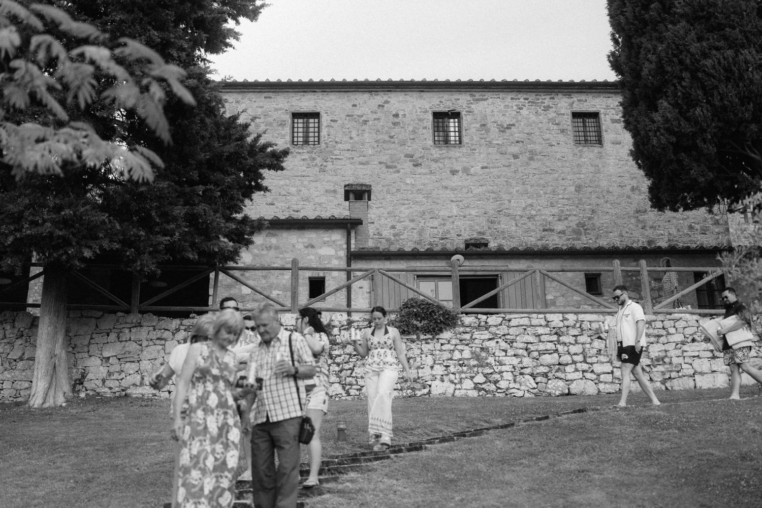 Guests socializing on the lawn of a rustic stone villa at an outdoor wedding in Tuscany.