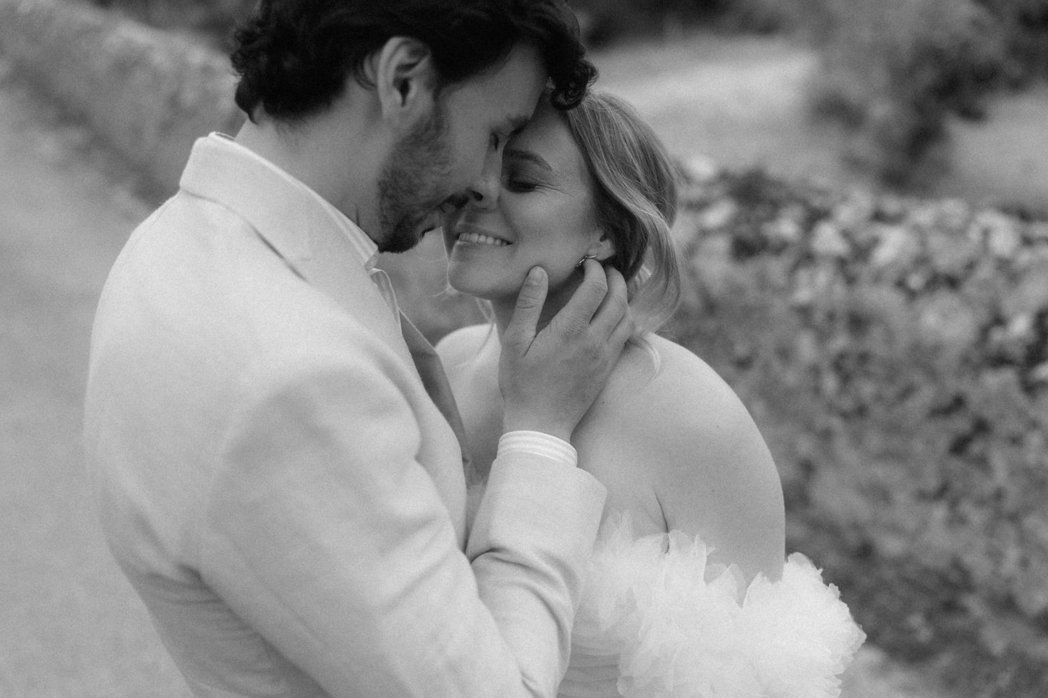 Black and white photo of a groom tenderly cradling his brides face as they share an intimate moment.