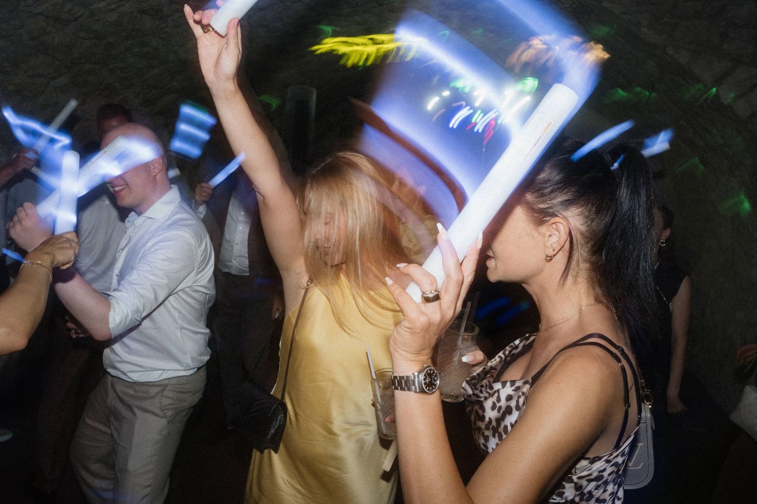 People dancing and holding glowing light sticks at an energetic nightclub party event.